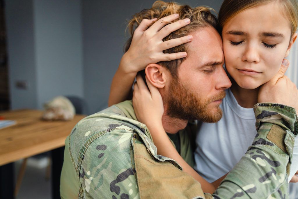Masculine military man hugging her crying daughter while kneeling